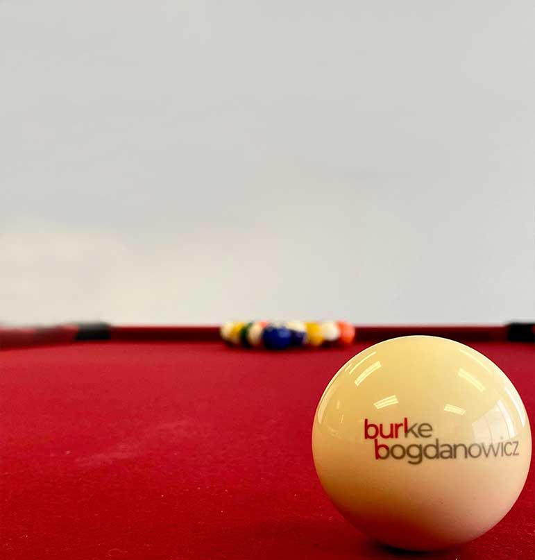 Cue ball with Burke Bogdanowicz logo on it on a red pool table with other balls in the background