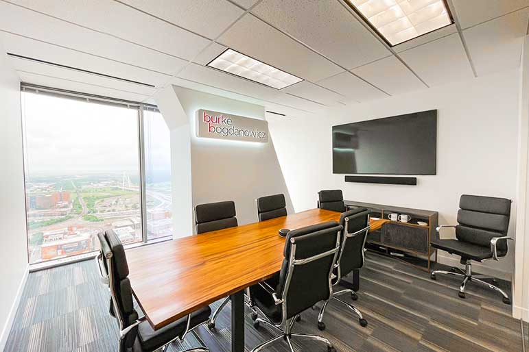 Burke Bogdanowicz meeting room. A wooden table with black leather chairs and a flat screen TV on the wall.